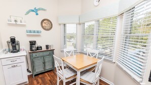 A kitchen with white cabinets, a coffee maker, and a dining table with chairs. - Oceanside, Community Pools, Community Tennis, Seasonal Community Trolley, M418, Mermaids Cove (Corolla)