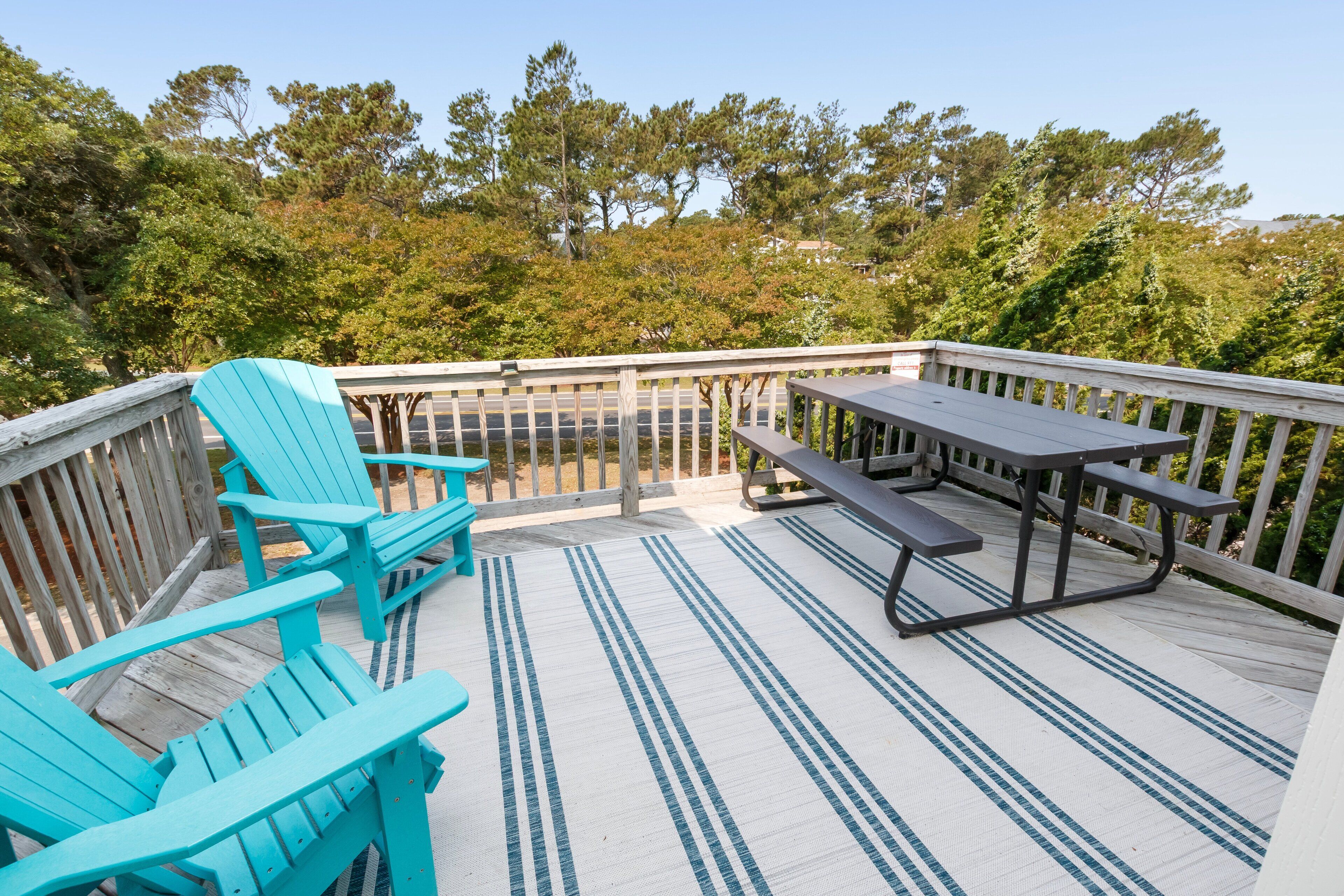 Une terrasse en bois avec une table de pique-nique et deux chaises Adirondack turquoise.