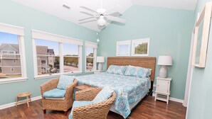 A bedroom with a large bed, wicker chairs, a small stool, and a ceiling fan. - Oceanside, Community Pools, Community Tennis, Seasonal Community Trolley, M418, Mermaids Cove (Corolla)