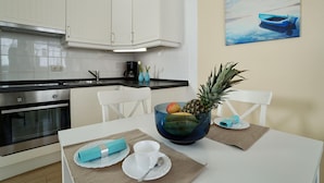 Eine moderne Küche mit weißen Schränken, einem Edelstahlbackofen und einer Essecke mit Tisch für zwei Personen.