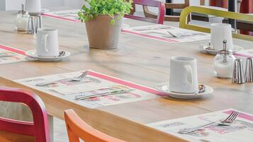 A dining table set with white plates, silverware, and a potted plant.