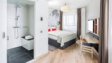 Ein modernes Hotelzimmer mit Dusche, einem Bett mit rotem Zierkissen, einem Schreibtisch und einer Wand mit einer Karte.