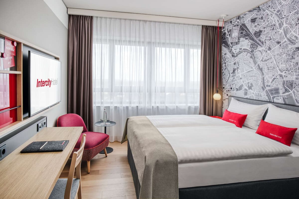 A hotel room with a bed, a desk, a chair, a TV, and a map wall.