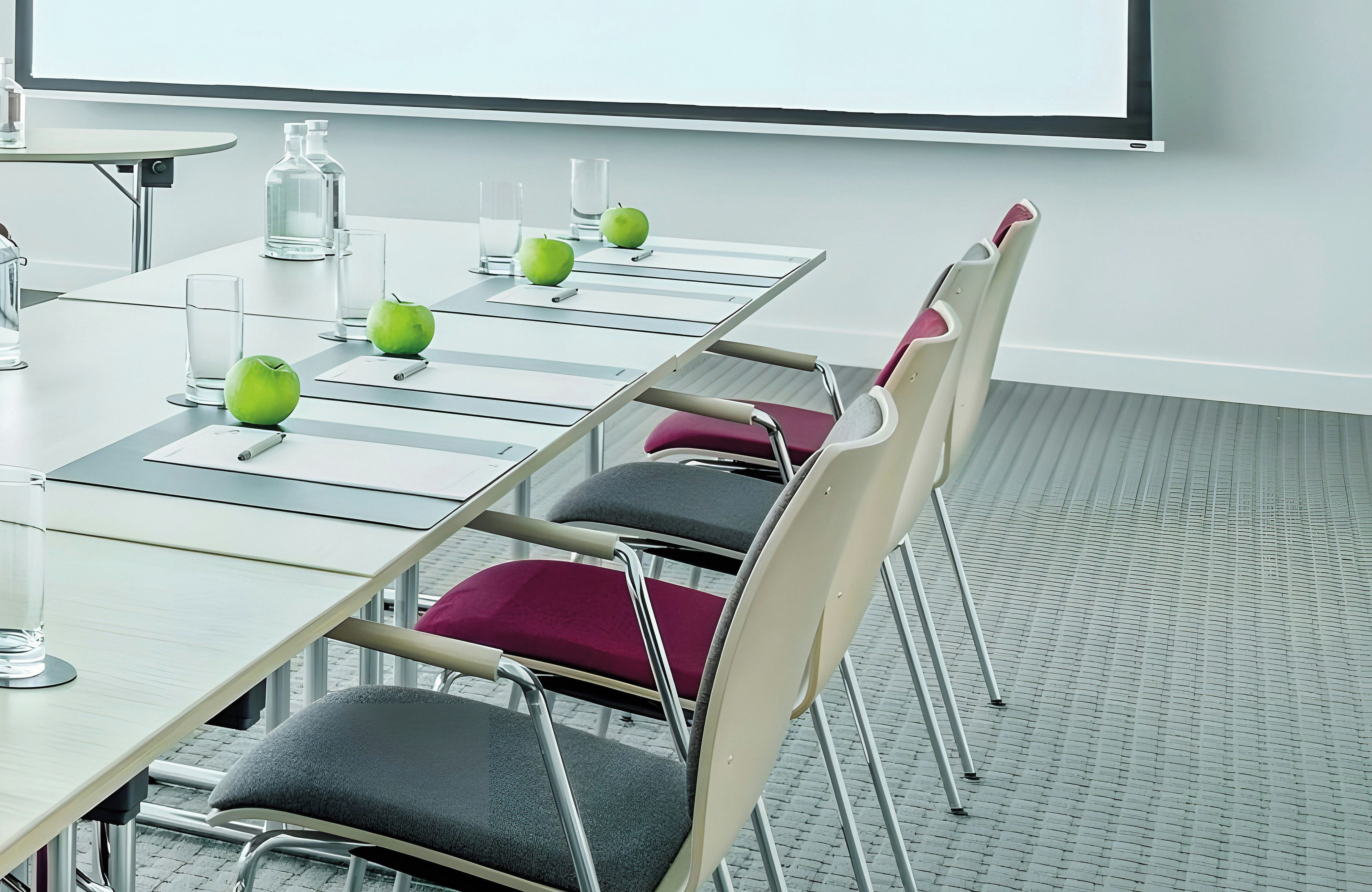 Een vergaderruimte met een lange tafel, stoelen, een projectiescherm en een waterdispenser.