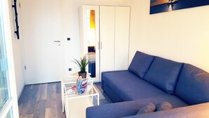A modern living room with a grey sofa, a glass coffee table with magazines, a potted plant, and a painting of a sailboat on the wall. - Urlaub und Erholung mit Charme und Stil auf Rügen (Sellin)