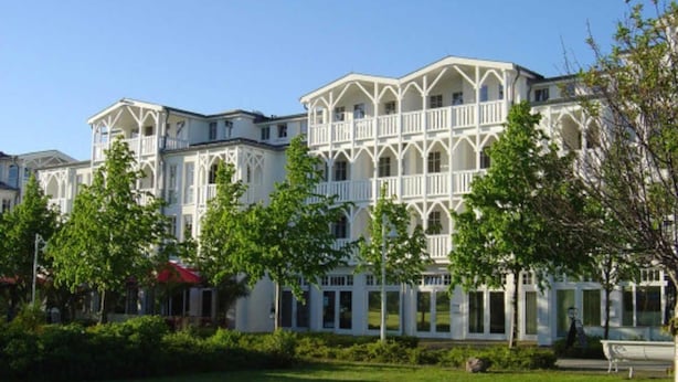 A large, multi-story building with a symmetrical facade, multiple balconies, and a well-maintained lawn in front. - Urlaub und Erholung mit Charme und Stil auf Rügen (Sellin)