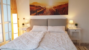 A bedroom with a large bed, two bedside tables, and a wall-mounted painting of a beach scene. - Urlaub und Erholung mit Charme und Stil auf Rügen (Sellin)