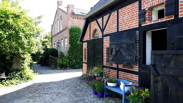 A cobblestone path leading to a traditional brick building with a black and white facade, a wooden bench, and potted plants. - Ferienwohnung "rosenrot" auf dem Ferien + Bauernhof Nilson in Inselmitte (Fehmarn)