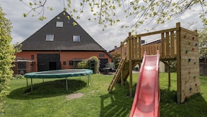 A playground with a slide and climbing wall, a trampoline, and a house in the background. - Ferienwohnung "rosenrot" auf dem Ferien + Bauernhof Nilson in Inselmitte (Fehmarn)