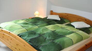 A single bed with a wooden frame, green and white bedding, and a bedside lamp.
