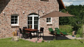 Una casa de ladrillo con un patio que incluye una mesa y sillas, un espacio de estar techado y un gran paraguas.