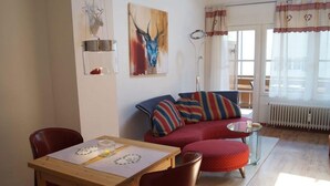 Ein gemütliches Wohnzimmer mit einer roten Couch, einem Holzespeisetisch mit Stühlen und einem Bild eines Rehs an der Wand.