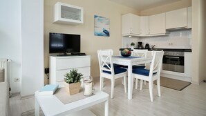 Una cocina moderna con armarios blancos, una mesa de comedor con sillas azules, un televisor sobre un mueble blanco y una cafetera.