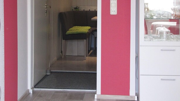Ein Zimmer mit Holzboden, einem weißen Kleiderschrank, einem Essbereich mit Tisch und Stühlen sowie einer Tür zu einem weiteren Raum.