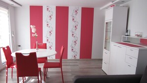 Ein modernes Wohnzimmer mit einem grauen Sofa, einem Esstisch mit roten Stühlen und einer Küchenzeile mit einem weißen Kühlschrank.