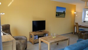 A living room with a TV, wooden furniture, and a painting on the wall. - Bispinger Heidezauber - Haus Hartriegel (Bispingen)