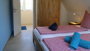 A bedroom with a wooden wardrobe, a bed with checkered bedding, a blue towel, and a bedside table with a lamp. - Bispinger Heidezauber - Haus Hartriegel (Bispingen)