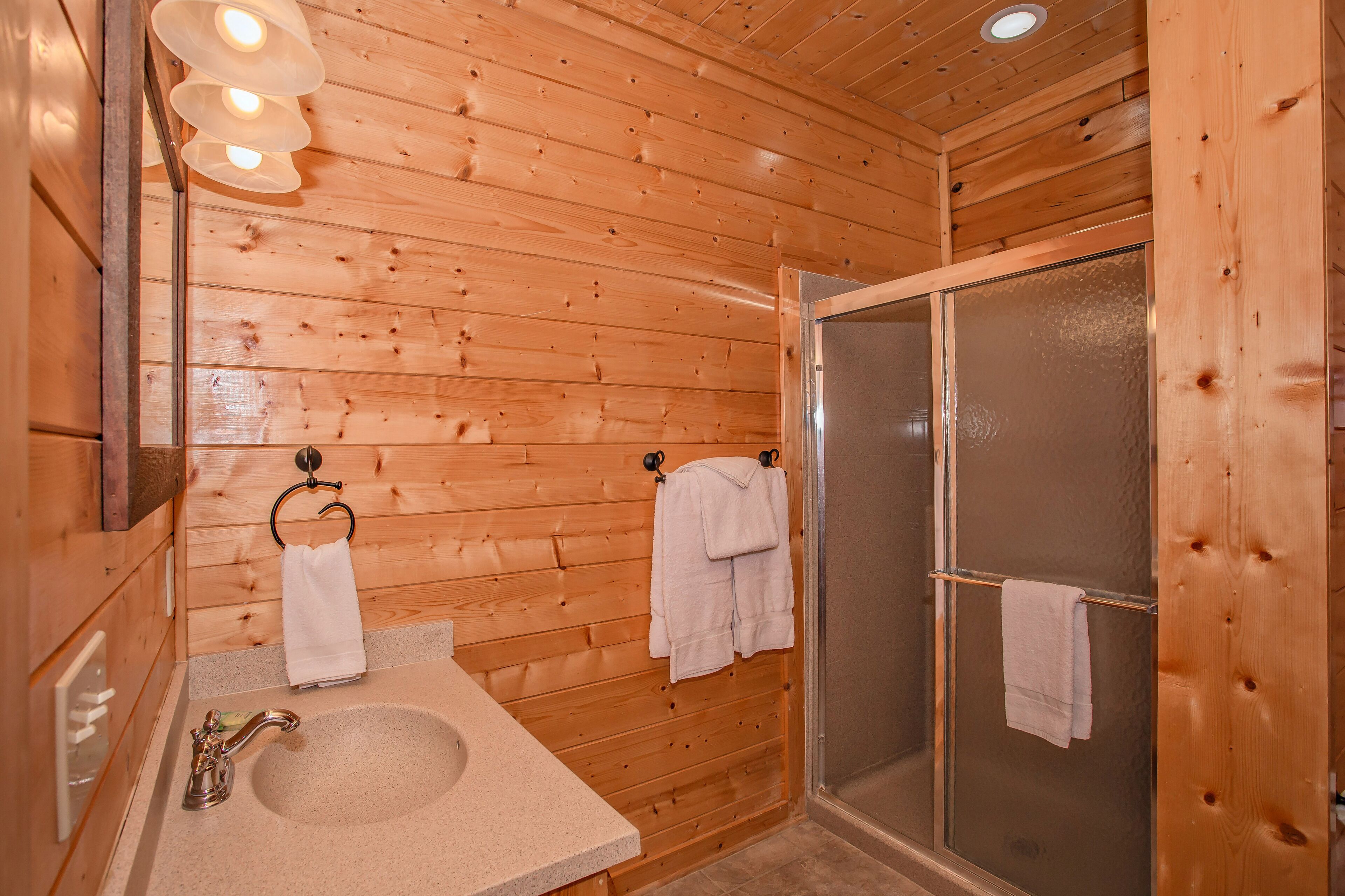 Une salle de bain rustique, aménagée dans une cabane en bois, avec un lavabo, un porte-serviettes et une douche en verre.