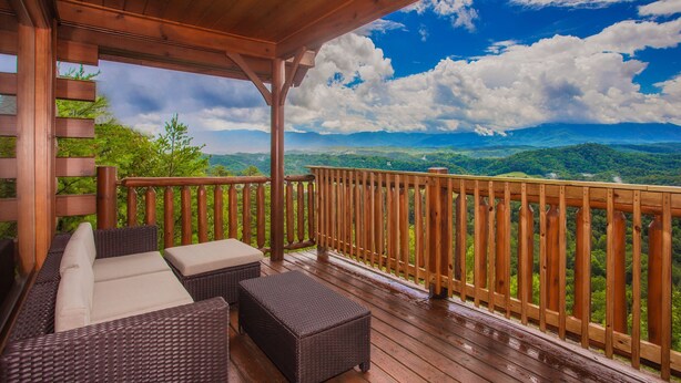 Terraza de madera con mobiliario de mimbre y vista a las colinas verdes.