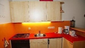 A compact kitchen with a red countertop, a sink, and basic cabinetry. - Falkenberg Wohnung 211 (Oberstdorf)