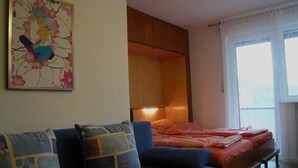Una stanza con un divano blu, un letto con coperta arancione, una testata del letto in legno e una finestra con tende.