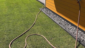 Un cortile con erba sintetica, un tubo da giardino e un barbecue.
