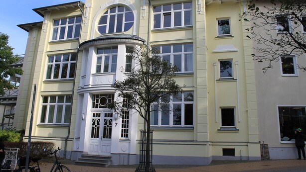 A multi-story building with a classic architectural style, featuring a prominent entrance with a white door and a large circular window above it. - Strandnahe Ferienwohnung im Ostseebad Göhren (Göhren)