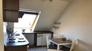 A compact kitchen with a window, a sink, a stove, and a dining area with chairs and a table. - Ferienwohnung Op'n Rugenbarg 70 (Cuxhaven)