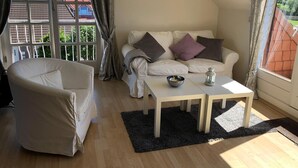 A cozy living room with a white sofa, a white armchair, and a small table with a bowl and a lantern. - Ferienwohnung Op'n Rugenbarg 70 (Cuxhaven)