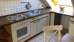 A kitchen with a gas stove, oven, and sink. There is a window with a view of the outside. - Ferienwohnung Op'n Rugenbarg 70 (Cuxhaven)