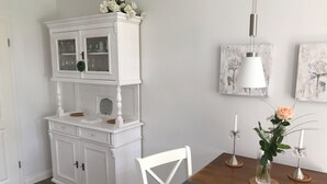 Un comedor con un armario blanco, una mesa de madera con manteles individuales estampados con motivos de estrellas y un florero con una sola rosa.