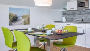 A modern kitchen with white cabinets, a wooden backsplash, and a dining area with a table set for two. - Penthouse-hafenwohnung Reeders Topp (Kappeln)