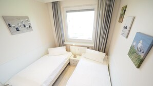 Una habitación pequeña y luminosa con dos camas individuales, una ventana con cortinas y algunas decoraciones en la pared.
