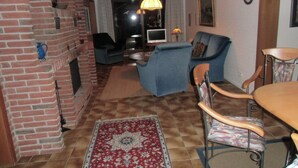 A living room with a brick fireplace, a blue sofa, a wooden dining table, and a patterned rug. - Haus Halligblick, Ferienwohnung Pellworm (Dagebuell)