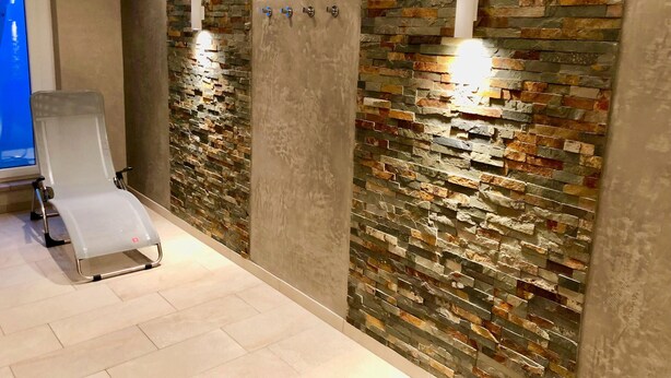 A modern bathroom with a stone wall, a white chair, and a light fixture. - Ankerplatz-sylt Haus Mateika - Wohnen Sie Exklusiv im Herzen von Westerland (Sylt)