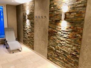 A modern bathroom with a stone wall, a white chair, and a light fixture. - Ankerplatz-sylt Haus Mateika - Wohnen Sie Exklusiv im Herzen von Westerland (Sylt)