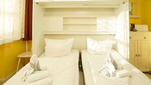 A hotel room with two beds, each with white linens and pillows, a small table, and a cabinet. - Sylter Strandgut, Haus Germania (Sylt)