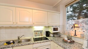 A kitchen with white cabinets, a granite countertop, a stove, a microwave, and a window with a view of trees. - Sylter Strandgut, Haus Germania (Sylt)