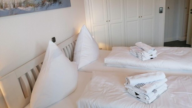 A hotel room with two beds, white bedding, and a beach-themed painting on the wall. - Nordmarkhof (Sylt)