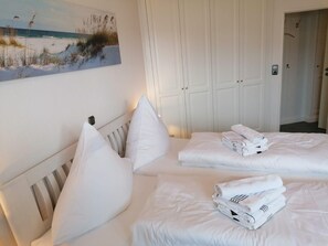 A hotel room with two beds, white bedding, and a beach-themed painting on the wall. - Nordmarkhof (Sylt)
