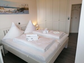 A hotel room with two beds, white bedding, a painting of a beach, and a wardrobe with a mirror. - Nordmarkhof (Sylt)
