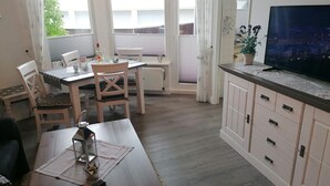 A dining area with a table, chairs, and a TV on a cabinet. - Nordmarkhof (Sylt)