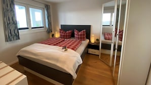 A bedroom with a bed, bedside tables, a mirror, and a window. - 2-zi-hafenwohnung Reeder's Nest Olpenitz (Kappeln)