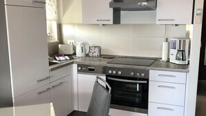A modern kitchen with white cabinets, a built-in oven, a coffee maker, and a clock on the wall. - Studioapartment "carpe Diem" (Kastela)