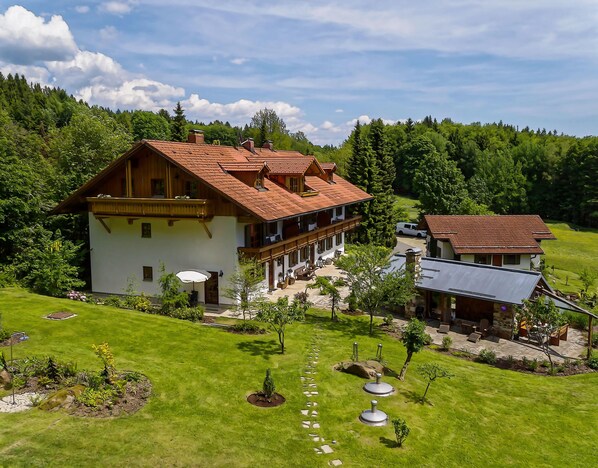 A large two-story house with a red-tiled roof, surrounded by lush greenery and a well-maintained lawn.