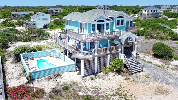A multi-story beachfront house with a pool, balconies, and a staircase leading to the beach.