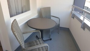 A small balcony with a round table and two wicker chairs. - App. Syltliebe, Haus Ankerlicht, Whg. 70 (Sylt)