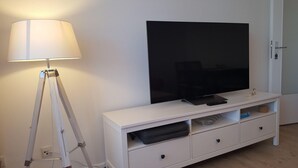 A white entertainment unit with a flat-screen TV, a lamp, and a few drawers. - App. Syltliebe, Haus Ankerlicht, Whg. 70 (Sylt)