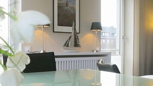 A modern room with a glass table, two chairs, a framed painting on the wall, and a view of buildings through a window. - Victoriaresidenz App. 12, Ekki' s Suite (Sylt)