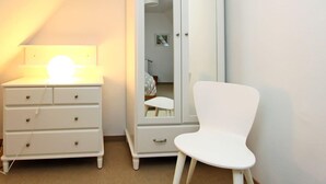 A bedroom with a white wardrobe, a bedside table with a lamp, and a white chair. - Lorenz (Hörnum (Sylt))